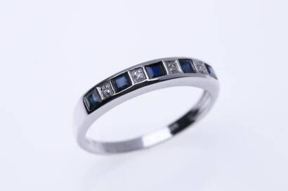 A sapphire and diamond eternity band, channel and grain set with five calibre sapphires and four round brilliant cut diamonds. 9ct white gold. Weight 2.04 grams. Size N. STAMPED 375.