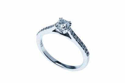 A diamond ring, the central cushion cut diamond claw set above diamond line shoulders.18ct white gold. Weight 3.29 grams. Size L ½. 