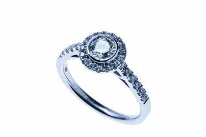 A diamond ring, the central modern brilliant cut diamond bezel set and surrounded by small brilliant cut diamonds. 18ct white gold. Weight 4.53 grams. Size N ½.