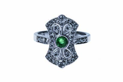 An emerald and diamond plaque ring, the pierced plaque set with a central round emerald and small round modern brilliant cut diamonds. 18ct white gold. Weight 6.4 grams. Size M½.