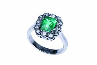 An emerald and diamond cluster ring, four claw set with a central rectangular step cut emerald of estimated weight 1.50 carats and surrounded by twelve modern round brilliant cut diamonds of total estimated weight 0.68 carat. 18ct white gold. Weight 5.10 