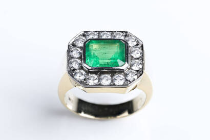 An emerald and diamond ring, of octagonal cluster design, the rectangular step cut emerald of estimated weight  3.25 carats, surrounded by fourteen brilliant cut diamonds of estimated total weight 1.68 carats. 18ct white and yellow gold. Weight 14.5 grams